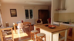 Cucina con isola in legno, sgabelli, tavolo da pranzo e sedie. Si nota una finestra con persiane, un termosifone e un fornello.