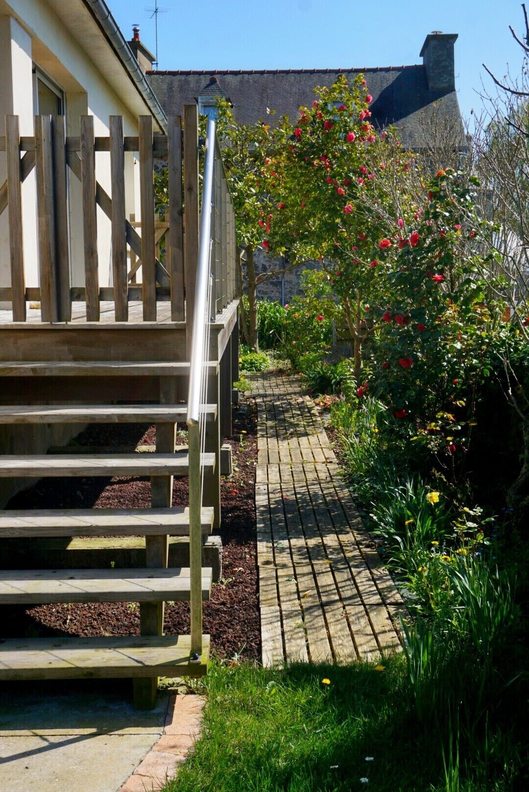 A wooden staircase leading to a building with a brick roof, surrounded by a garden with various plants and flowers.