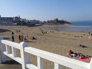 A beach with people sunbathing and swimming, a white fence, and buildings in the background. - Bright, family-friendly house, close to beaches and shops (Saint-Quay-Portrieux)