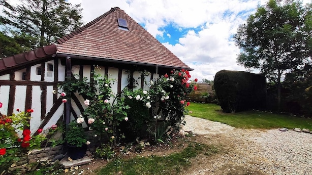 Une maison traditionnelle à colombages, dotée d’un toit en pente et d’un jardin agrémenté de plantes à fleurs.