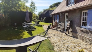 Une terrasse dallée de pierres, aménagée avec du mobilier d’extérieur, un hamac et un barbecue.