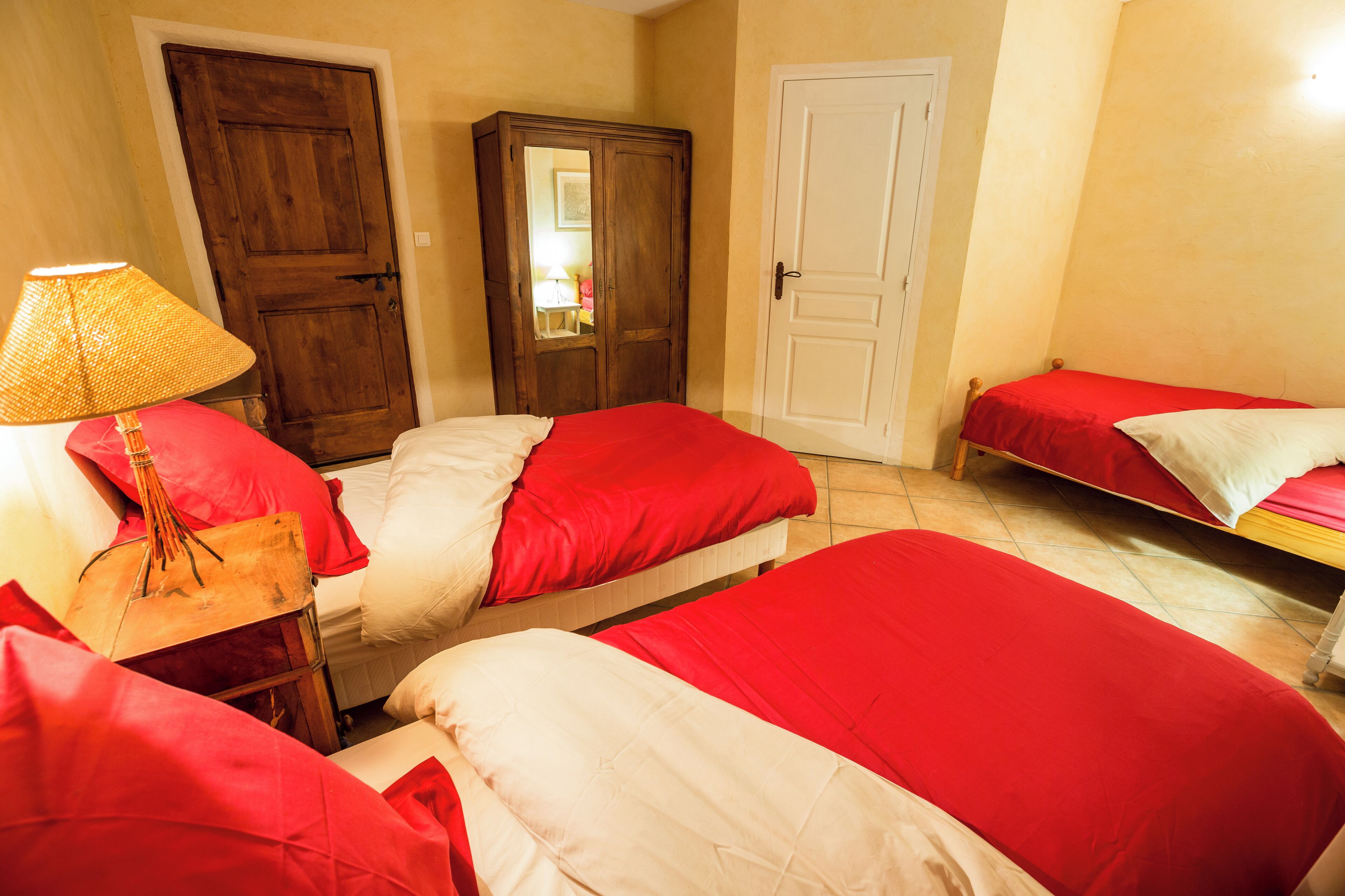 A bedroom with two beds, a wooden wardrobe, a lamp, and a door.