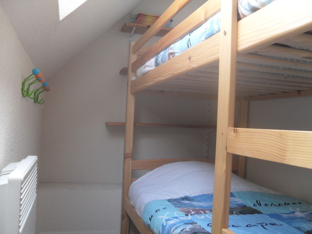 A bunk bed with a white mattress and a blue cover with text. There is a white radiator on the left and a shelf with books above the bed.