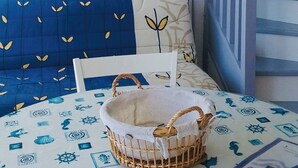 Una stanza con un divano blu, una parete bianca con due quadri, una lampada da terra blu e un cesto su un tavolo ricoperto da una tovaglia a tema nautico.