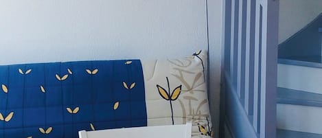 Huoneessa on sininen sohva, valkoinen seinä, jossa on kaksi taulua, sininen lattiavalaisin ja pöydällä kori, jonka päällä on meriaiheinen pöytäliina.
