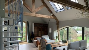 Amplio salón con techos altos, vigas de madera a la vista, un ventanal grande y una zona de estar acogedora.
