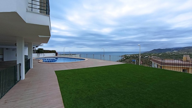 Um edifício moderno com piscina, área gramada e vista para o mar.
