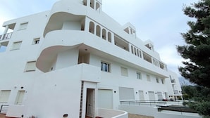Um edifício moderno e branco com várias varandas, entrada com portão e acesso por caminho de cascalho.