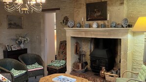 A cozy living room with wicker furniture, a fireplace, and a chandelier. - Pretty stone house, 3 bedrooms, 2 bathrooms with a large enclosed garden (Longues-sur-Mer)