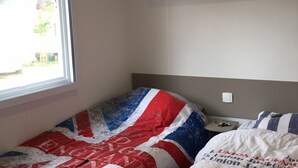 Une chambre à coucher avec un lit recouvert d’une couverture ornée du drapeau Union Jack, une fenêtre avec des stores et une étagère au-dessus du lit.