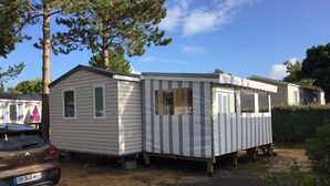 Une maison mobile avec un petit garage attenant, une voiture garée devant, et un ciel dégagé.