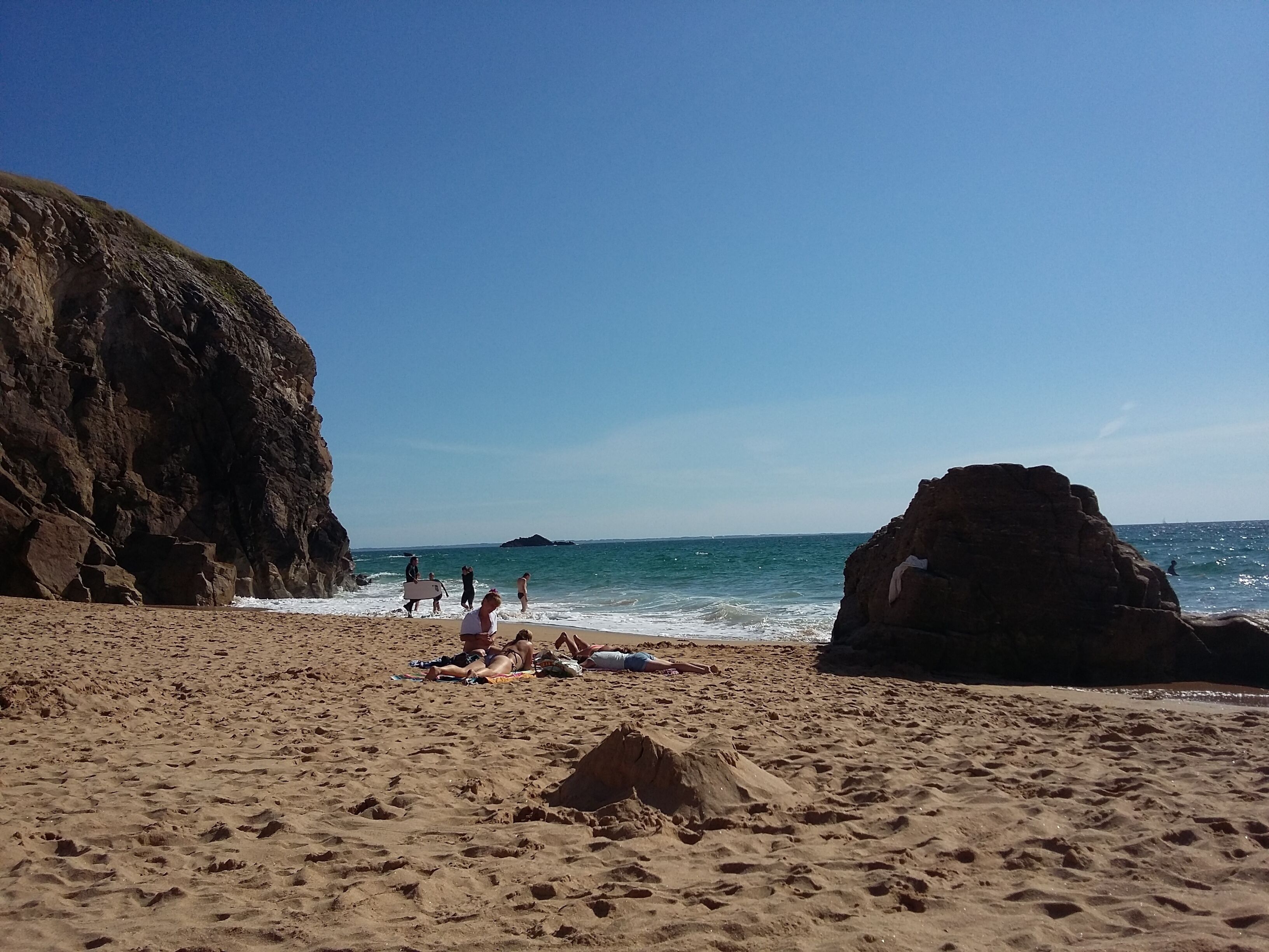 Ein sandiger Strand mit Felsformationen und einem klaren, blauen Himmel.