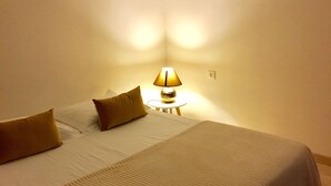 A neatly made bed with a white and beige bedspread, two pillows, and a small bedside table with a lamp.