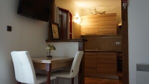 A compact kitchen with wooden cabinets, a built-in stove, and a dining area with two chairs and a small table.