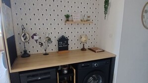 A compact kitchen with a washing machine, a wooden countertop, and a patterned wall.