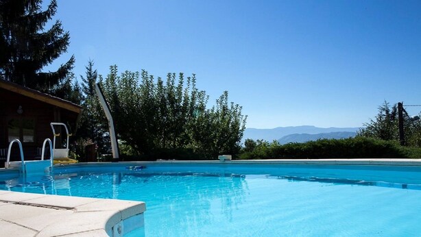 A clear blue pool with a wooden deck, a lifeguard stand, and a view of mountains in the background.