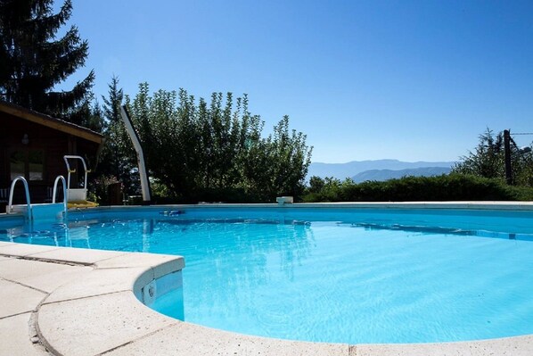 A clear blue pool with a wooden deck, a lifeguard stand, and a view of mountains in the background.