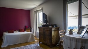 A bedroom with a bed, a wooden dresser, a table with a picture frame, and a window with a view.