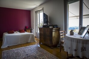 A bedroom with a bed, a wooden dresser, a table with a picture frame, and a window with a view.