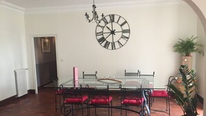Ein Essbereich mit einem Glastisch, schwarzen Metallstühlen und einer großen Wanduhr.