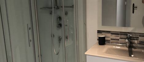 Ein modernes Badezimmer mit einer gläsernen Dusche, einem weißen Waschtisch mit Spiegel und einem Waschbecken.
