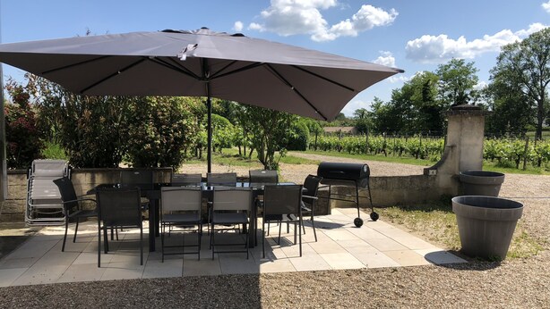Eine Terrasse im Freien mit Tisch, Stühlen, einem Grill und einem großen Sonnenschirm.