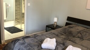 Ein Zimmer mit einem Bett, zwei weißen Handtüchern, einem Nachttisch und einem Spiegel.