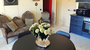 A dining area with a round table, chairs, a chandelier, a sofa, and a kitchen area with cabinets and a microwave. - "LA DAME AU BALCON" on the village square (Roussillon)