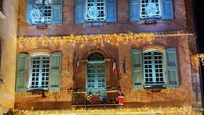 A two-story building with a central entrance, multiple windows with shutters, and a balcony with plants. - "LA DAME AU BALCON" on the village square (Roussillon)