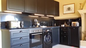 A modern kitchen with dark cabinetry, a built-in oven, a washing machine, and a coffee maker. - "LA DAME AU BALCON" on the village square (Roussillon)