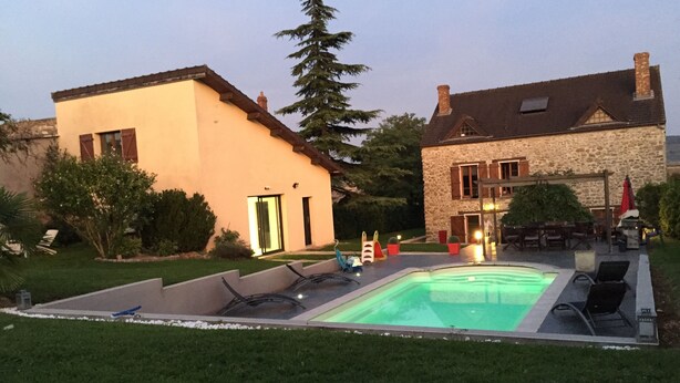 Un espace piscine avec des chaises longues, un bâtiment en pierre et une maison moderne avec une porte verte.