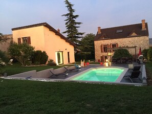 Uma área de piscina com espreguiçadeiras, um edifício de pedra e uma casa moderna com porta verde.
