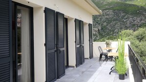Un balcon offrant une vue sur un paysage montagneux, avec une table, des chaises et un pot de fleurs.