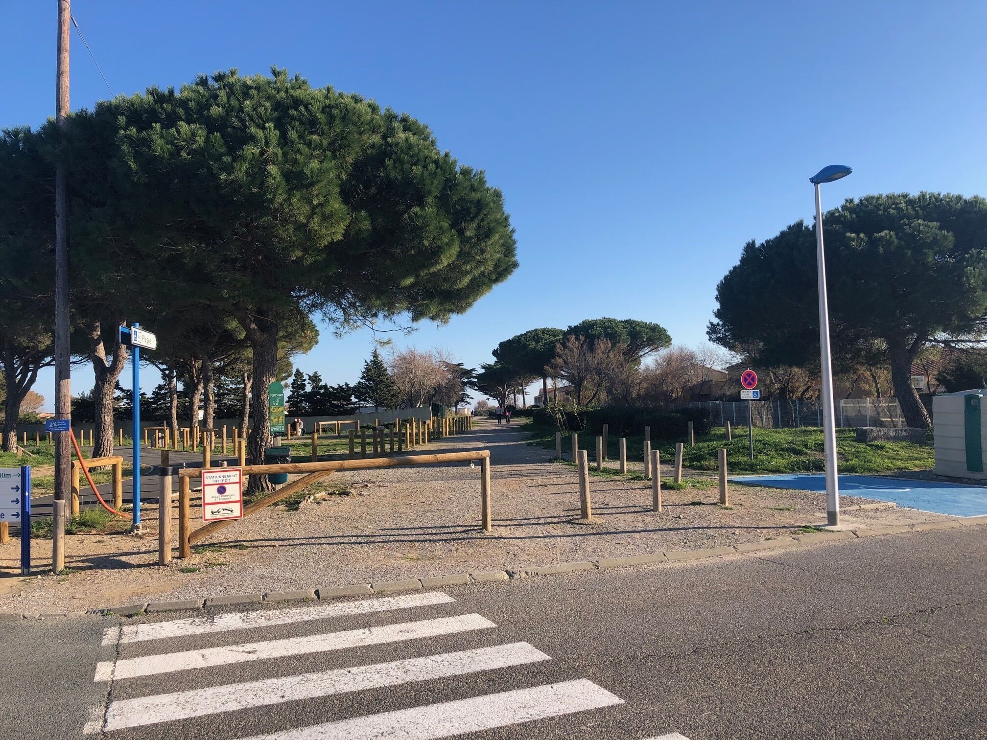 A crosswalk leading to a gated entrance with a wooden fence and trees.