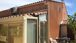 A building with a tiled roof, a sliding glass door, and a small patio with plastic chairs. - Holiday home - Gruissan les Ayguades - 6 people (Gruissan)