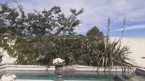 A pool with a stone sculpture, surrounded by lush greenery and a clear sky.