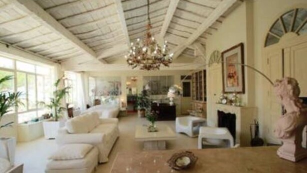 A spacious living room with a high ceiling, a chandelier, and a fireplace. There are several pieces of furniture including sofas and a coffee table.