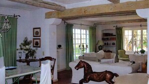 A traditional room with a wooden beam ceiling, a green curtain, a white sofa, a wooden horse sculpture, and a table with chairs.