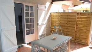 An outdoor patio with a table and chairs, a wooden fence, and a door leading to a covered area. - LAST MINUTE T2 N ° 2 HC (Cavalaire-sur-Mer)