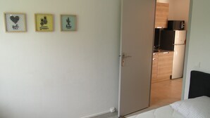 A bedroom with a bed, a door leading to a kitchen, and three framed pictures on the wall. - LAST MINUTE T2 N ° 2 HC (Cavalaire-sur-Mer)