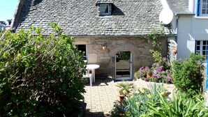 Ein Steinhaus mit Ziegeldach, einem kleinen Fenster und einem Garten mit verschiedenen Pflanzen und Blumen.