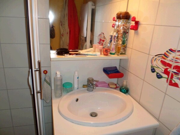 A bathroom with a white sink, a mirror, and various toiletries on the countertop. - Petite Maison de Pecheur on the Pink Granite Coast (Trébeurden)