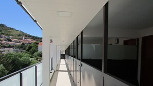 A corridor with large windows, a tiled floor, and a view of a hillside with buildings.