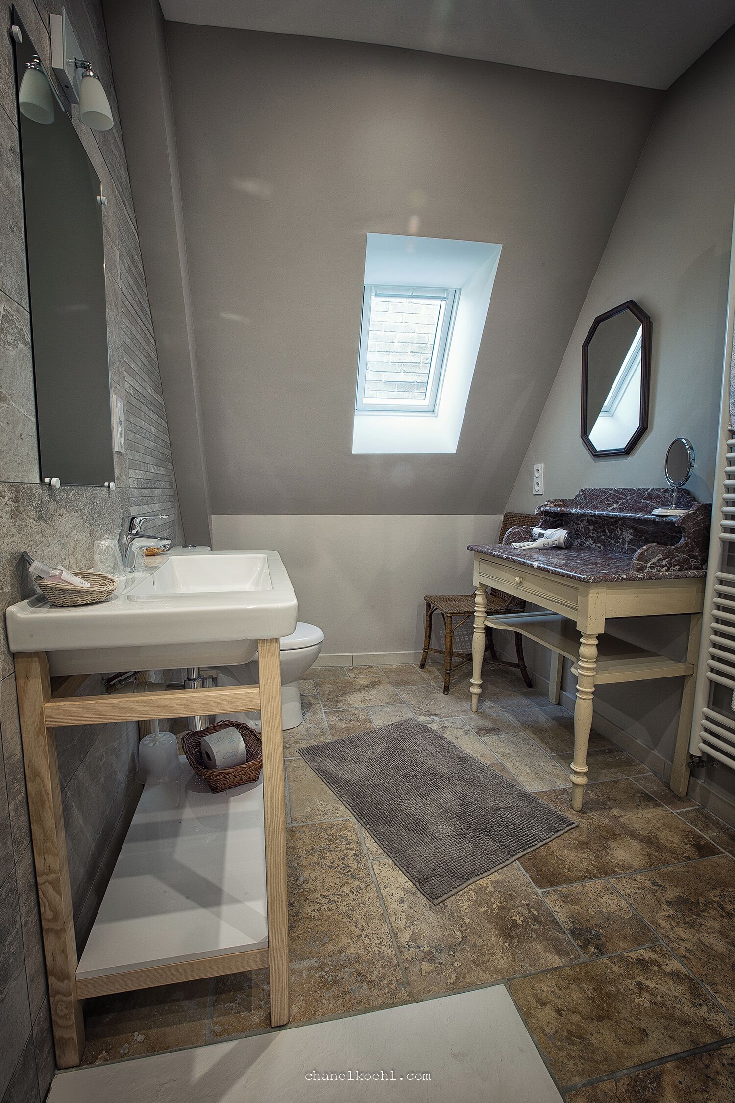 Une salle de bain avec un puits de lumière, un lavabo blanc, un meuble-lavabo avec un miroir et un banc en bois.