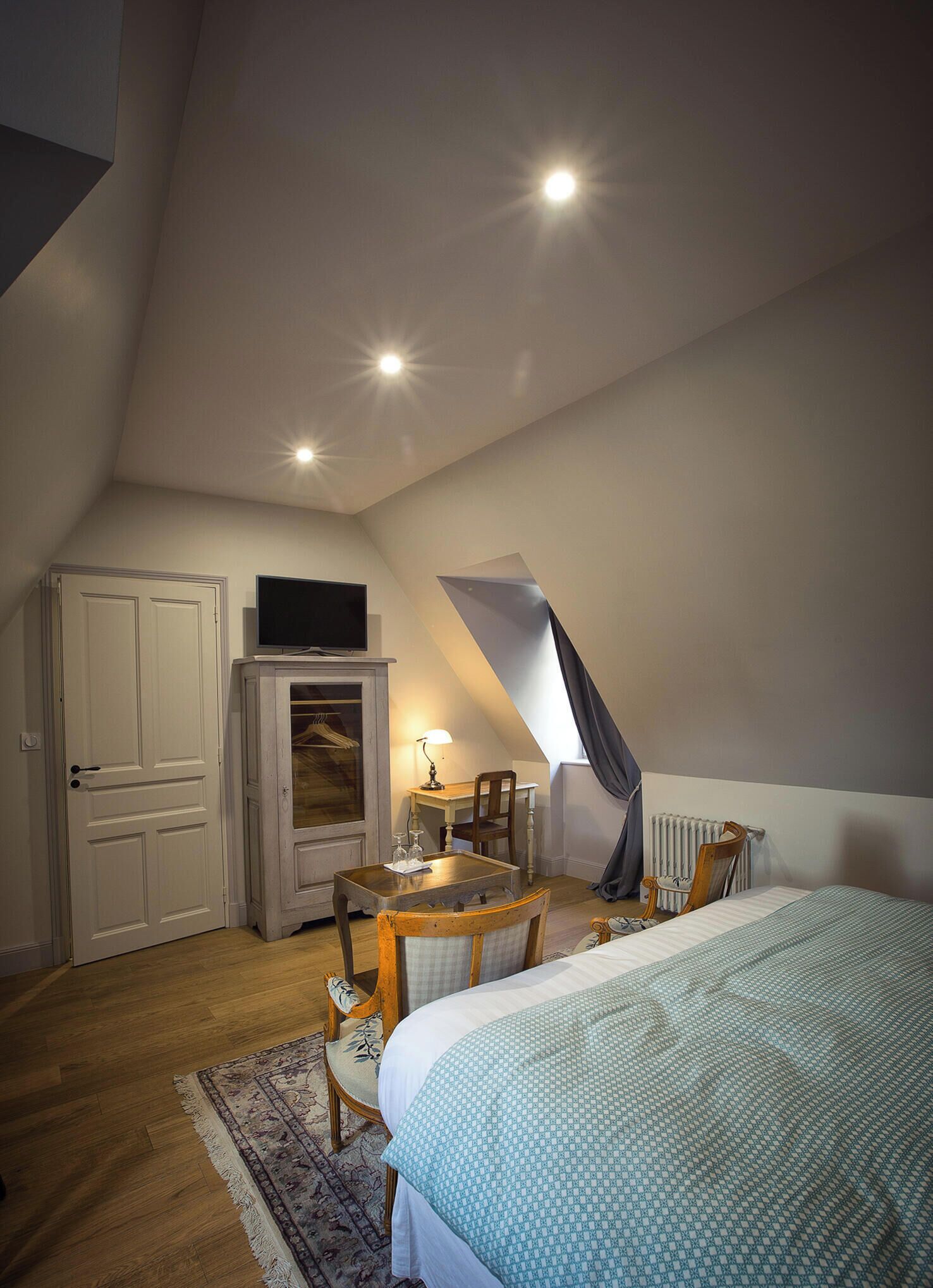 A bedroom with a bed, a desk, a chair, a television, and a radiator.