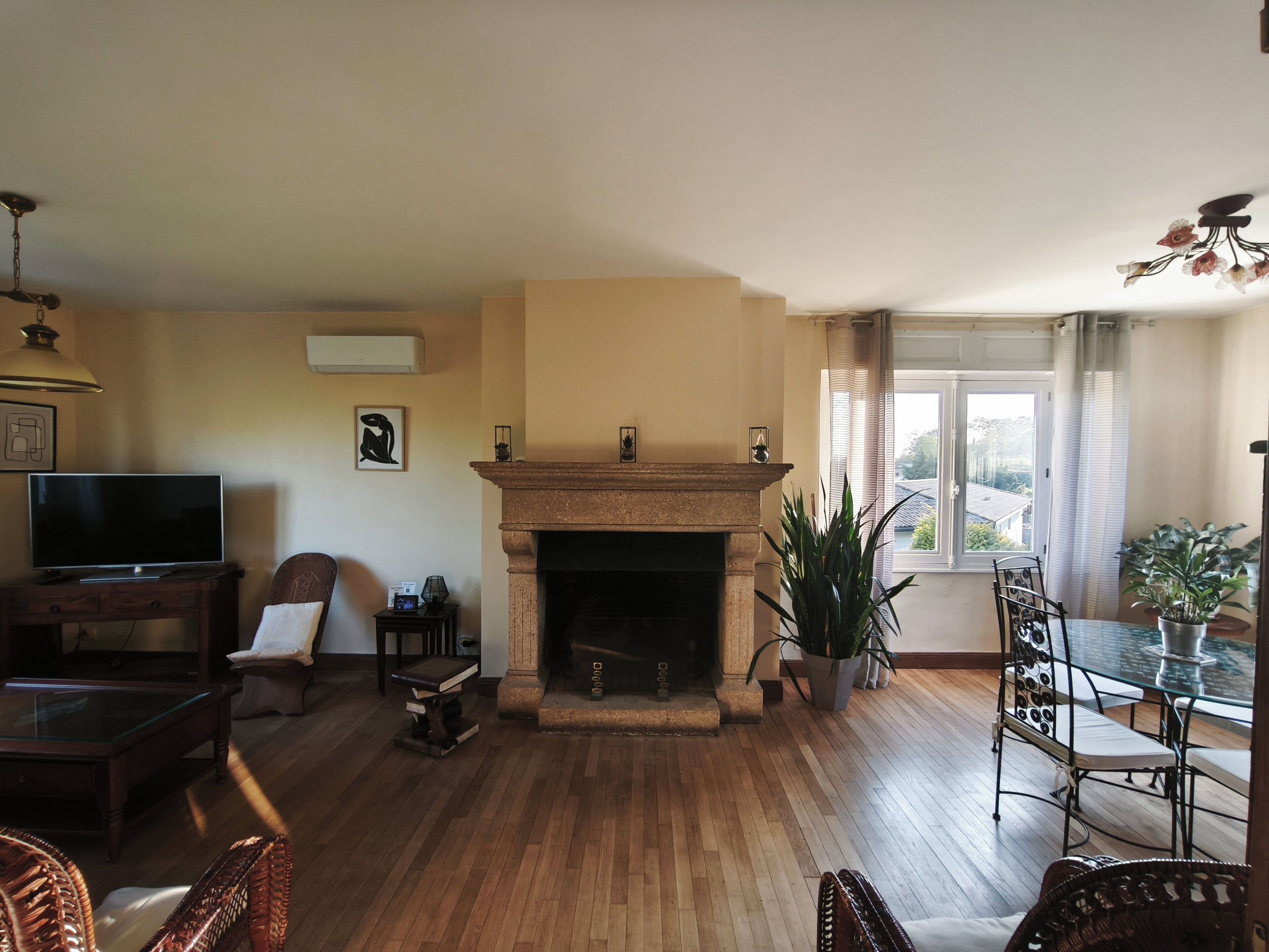 A living room with a fireplace, wooden flooring, a television, and a dining area with chairs.