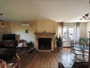 Ein Wohnzimmer mit Kamin, Holzboden, Fernseher und einem Essbereich mit Stühlen.