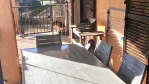 Portico esterno coperto con tavolo e sedie, un barbecue e vista su un paesaggio montano.