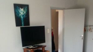 Un soggiorno con una televisione su un mobile in legno, un tappeto decorato, un divano grigio e una porta che dà su un'altra stanza.