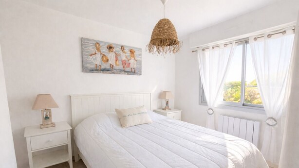 A bedroom with a bed, two bedside tables, a hanging lamp, a painting, and a window with curtains. - F2 250 m from the beach of Chay Royan (Royan)
